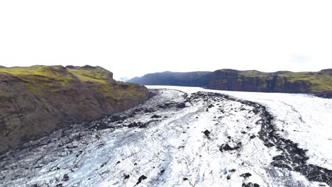 aerial-drone-view-of-an-impressive,-gigantic-glacier-in-volcanic-rock-on-the-island-of-Iceland,-with-mountains-on-its-sides