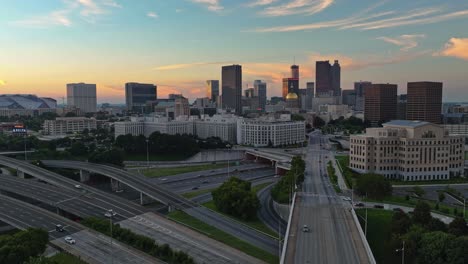 Disparo-De-Drone-Hiperlapso-De-Una-Autopista-Muy-Frecuentada-E-Iluminación-Del-Moderno-Horizonte-De-La-Ciudad-De-Atlanta-En-Segundo-Plano-Durante-La-Puesta-De-Sol-Dorada---Disparo-De-Drone-Panorámico