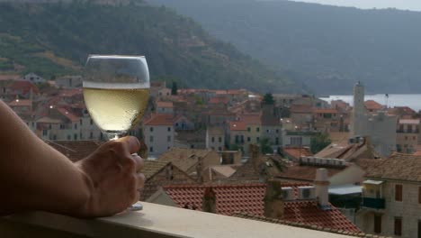 Woman-drinking-wine-on-balcony-with-view-of-seaside-town,-Komiza,-Croatia