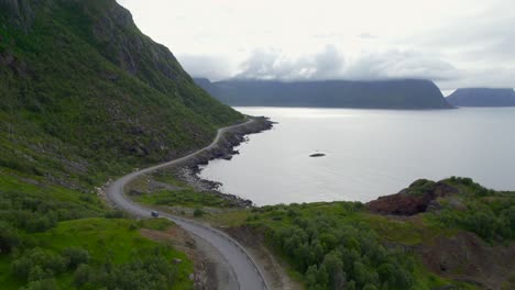 Aerial-dolly-shot-of-a-car-driving-along-the-scenic-highway-with-steep-dramatic-mountains-along-the-coast-in-Northern-Norway-in-the-summer-time
