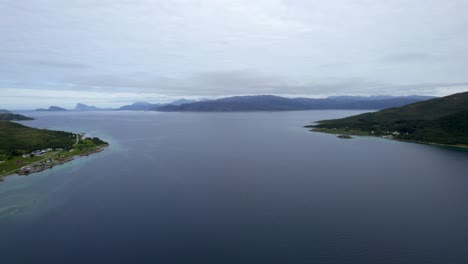 Reversing-aerial-dolly-shot-across-the-waterway-between-the-islands-of-kvaløya-and-Senja-on-a-slightly-overcast-day-with-a-small-boat-traveling-across-the-water