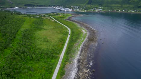 Aerial-dolly-forward-shot-of-the-famous-scenic-route-through-Senja-Norway-in-the-summer-with-green-scrub-forest-and-small-town-on-the-coast-of-a-fjord