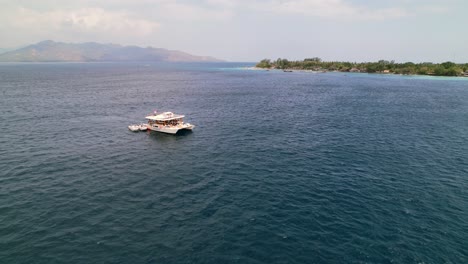 Catamaran-Yacht-Party-Boat-Cruising-near-Gili-Islands-on-Sunny-day-with-tourists-in-Indonesia---Aerial-Flyover