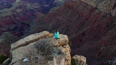 Woman-Standing-On-Edge-Of-A-Cliff-In-The-Grand-Canyon-National-Park-In-Arizona,-USA---aerial-shot