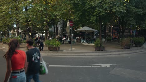 Friends-walk-past-outdoor-garden-cafe-in-downtown-urban-European-town