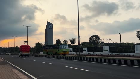 Denkmal-Mit-Uhr-Auf-Der-Asian-Avenue-Bei-Sonnenuntergang,-Vorbeifahrender-Shuttle,-Indien