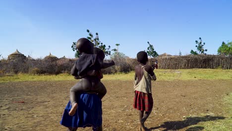 Niña-Cargando-A-Un-Bebé-Mientras-Caminaba-Hacia-La-Aldea-De-La-Tribu-En-Uganda,-África