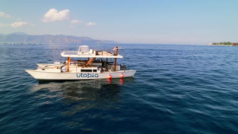 Asian-Woman-in-Swimwear-on-Rooftop-of-Catamaran-Yacht-Cruising-in-the-Gili-Islands---aerial-pull-back