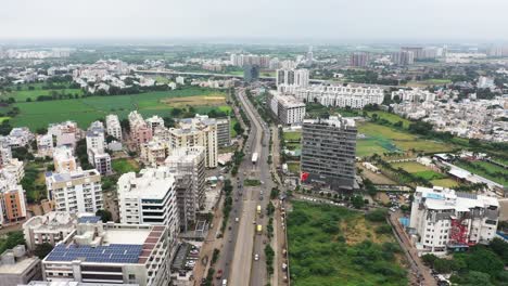 Die-Hintere-Drohnenkamera-Bewegt-Sich-über-Die-Ringstraße,-Die-Durch-Die-Von-Wolkenkratzern-Umgebene-Stadt-Rajkot-Führt