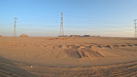 Desert-dunes-with-pyramids-in-backgrounds-behind-pylons-on-sandy-dusty-landscape