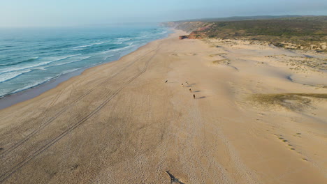 Luftaufnahme-Einer-Gruppe-Von-Pferden,-Die-Bei-Sonnenuntergang-Am-Ufer-Des-Strandes-Von-Bordeira-In-Portugal-Reiten