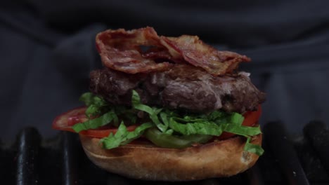 A-chef-assembling-a-meat-hamburger-with-bacon-lettuce-and-tomato,-on-the-grill