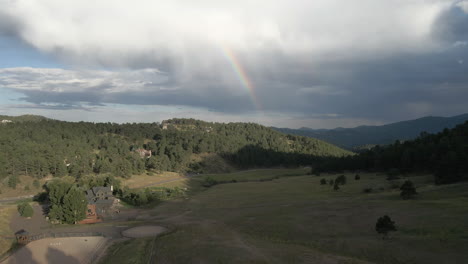 Fliegen-Sie-über-Bäume-Und-Berge-Mit-Einem-Regenbogen-Im-Hintergrund-In-Colorado,-Vereinigte-Staaten