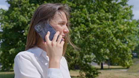 Woman-in-white-elegant-shirt-talking-on-phone,-windy-outdoors-weather