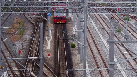 Red-single-car-train-slowly-running-on-train-tracks-and-moving-closer-to-view-and-disappears-past-the-camera