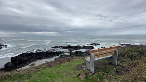Empty-Wooden-Bench-Over-The-Rocky-Shoreline-During-Sunrise