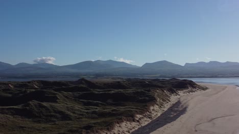 Aerial-view-rising-over-Newborough-beach-sand-dune-coastline-and-seascape-with-misty-ethereal-Snowdonia-mountain-range-skyline