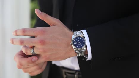 Groom-slowly-adjusting-silver-ring,-silver-Rolex-watch-reflecting-light