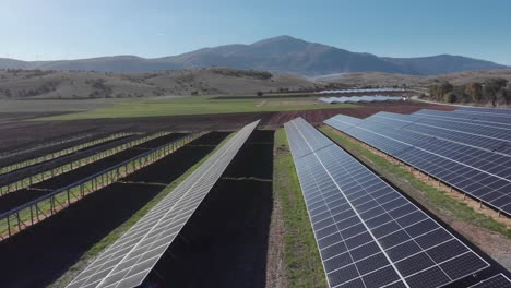 Drone-dolly-shot-over-renewable-energy-photovoltaic-solar-power-park-row-panels-background-mountains