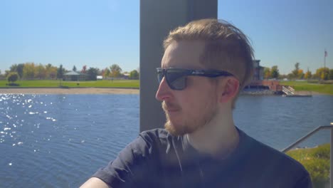 A-man-with-sunglasses-sits-at-a-lake-looking-across-the-water