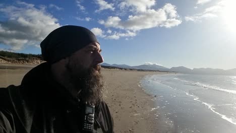 Active-bearded-male-observing-windy-island-seascape-ocean-waves-at-sunrise