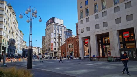People-walking-in-Piazza-San-Babila,-and-its-famous-shops-on-a-sunny-day