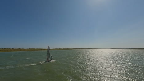 Aerial-tracks-catamaran-sailboat-heeling-into-onshore-waves-at-sea