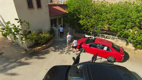 Toma-Aérea-De-Seguimiento-De-Hombres-Saliendo-Del-Auto-Y-Entrando-A-Casa-En-Un-Día-Soleado.