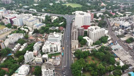 Eine-Luftdrohnenkamera-Fliegt-über-Die-Stadt-Rajkot-Und-Man-Sieht-Fahrzeuge,-Die-Von-Der-Überführungsbrücke-Herabsteigen