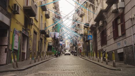 Narrow-street-with-driving-car-and-scooter-in-Naples-with-football-color-flags