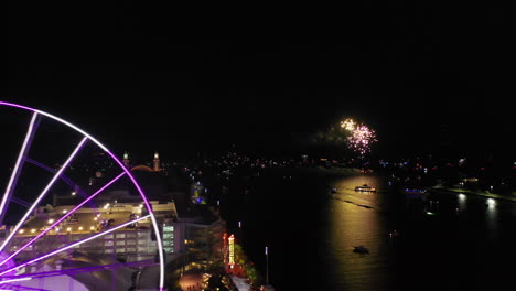 Aerial-tracking-shot-of-the-illuminated-Centennial-Wheel-revealing-fireworks-on-Lake-Michigan,-night-in-Chicago,-USA