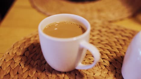 Nahaufnahme-Von-Kaffee-In-Weißer-Tasse,-Tischset-Aus-Korbgeflecht,-Gemütlicher-Morgen