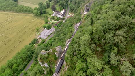 Aerial-view-of-a-small-steam-train-carrying-tourists,-in-the-middle-of-a-cliff,-in-the-Martel-region-in-summer,-Dordogne,-France
