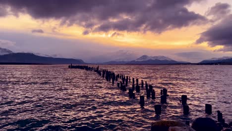 Relaxing-view-of-the-old-wooden-pier-of-Puerto-Natales-with-snowed-peaks-and-sunset-clouds-as-the-background,-Chilean-Patagonia-2023,-Chile