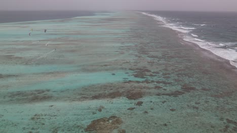 Aerial-time-hyper-lapse-over-fringing-reef-as-kite-surfers-coast-in-ocean-water-of-los-roques