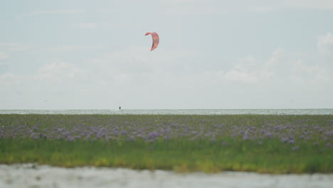 Static-wide-shot-of-a-kite-surfer-surfing-on-the-water-from-left-to-right-on-a-sunny-day
