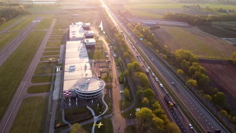 Drone-tilt-shot-of-Breda-International-Airport-next-to-a-busy-highway-during-sunset