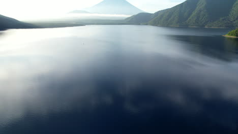 From-a-high-angle,-the-camera-tilts-upward,-unveiling-the-serene-expanse-of-Lake-Motosu-and-the-iconic-grandeur-of-Mount-Fuji