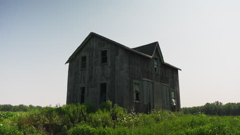 Abandoned-wooden-house-in-grassy-field-of-flowers,-space-for-text,-establishing