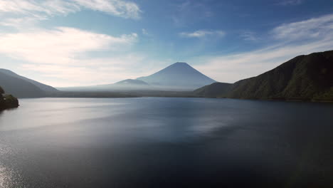 Luftvergnügen-Der-Anmutige-Rückzug-Einer-Drohne-Zeigt-Den-Motosu-See-Mit-Dem-Ikonischen-Berg-Fuji,-Der-Majestätisch-Den-Hintergrund-Dominiert