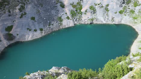 Aerial-view-over-a-man-standing-at-a-viewpoint,-overlooking-the-Blue-lake-in-sunny-Imotski,-Croatia