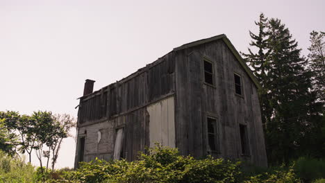 Profile-backlit-view-of-abandoned-wooden-cabin-broken-windows,-grey-wood