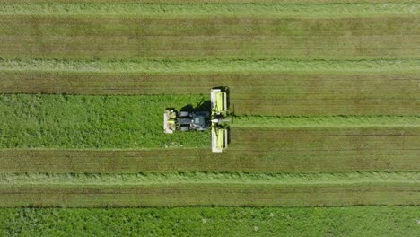 Aerial-establishing-view-of-a-tractor-mowing-a-fresh-green-grass-field,-a-farmer-in-a-modern-tractor-preparing-food-for-farm-animals,-sunny-summer-day,-wide-birdseye-drone-dolly-shot-moving-left