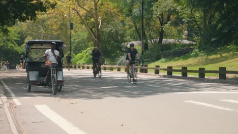 Ciclistas-Y-Scooters-Recorren-Un-Sendero-En-Central-Park-Mientras-Los-Taxis-En-Bicicleta-Avanzan-Por-La-Costa.