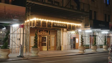 Front-entrance-of-Warwick-hotel,-gentle-yellow-neon-glow-from-string-lights-above