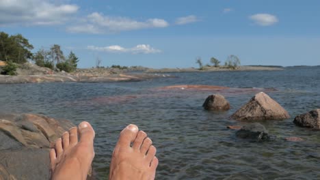 Bare-feet-on-rocky-shore-sea-island-in-summer,-point-of-view