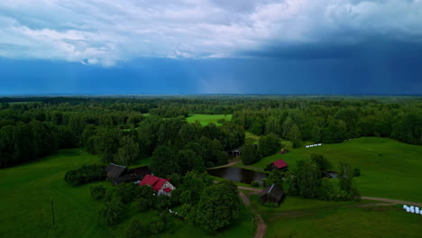 Drone-descends-tilt-down-to-farm-house-in-middle-of-forested-countryside-in-stormy-day