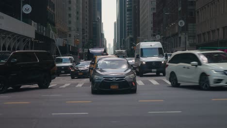 Cars-creep-forward-turning-onto-road-in-skyscraper-lined-street