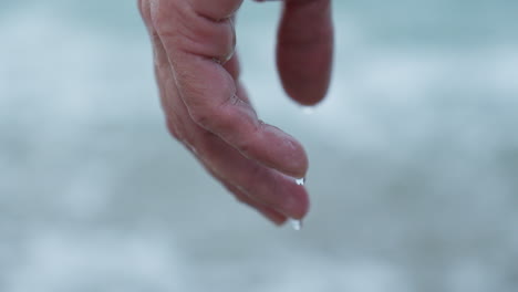 Close-Up-of-Water-Dripping-from-Man's-Hand-on-Grey-Morning-Beach