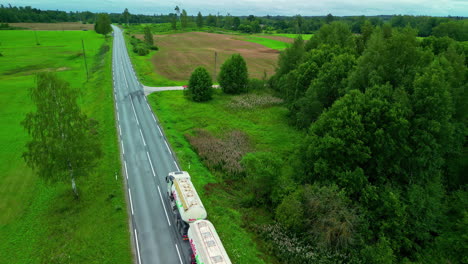 Tanker-truck-driving-down-a-country-road-in-summer---aerial